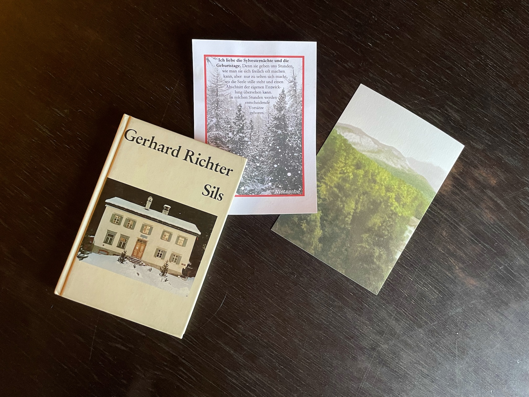 左から「Sils」展のカタログ、リヒターの作品の上にニーチェの言葉をのせたニーチェ・ハウスのポストカード、シルス・マリアの高級ホテル、ヴァルドハウスからの眺めを描いたリヒターの作品によるポストカード。